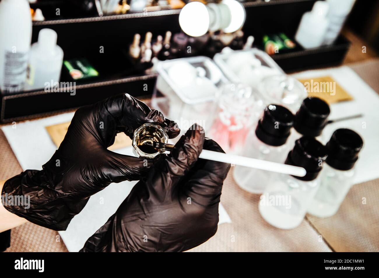 Arbeitsplatz eines Meisters der Augenbraue und Make-up-Künstler. Die Hände des Meisters in schwarzen Handschuhen halten einen Behälter mit Make-up-Flüssigkeit und einer Bürste. Stockfoto