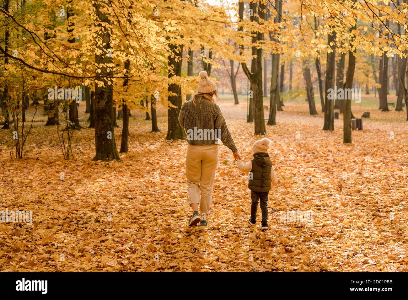 Die junge Mutter mit ihrem Sohn genießt einen schönen Herbsttag und einen Spaziergang im Park. Goldenes gelbes Laub, das die Hände hält. Foto in vollem Wachstum, Ansicht aus dem Stockfoto