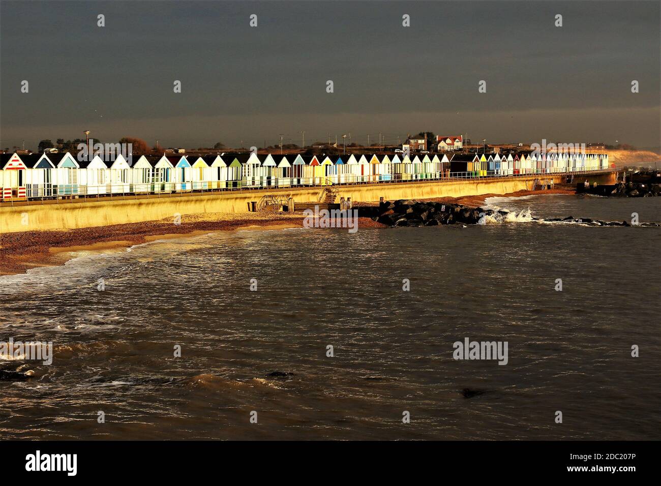 Sturmwolken bedrohen eine Reihe von Strandhütten, während die Die Sonne scheint weiter Stockfoto