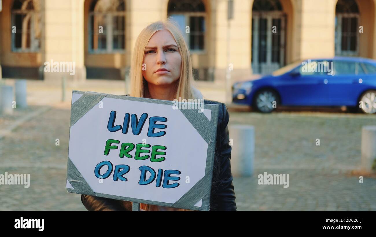 Frau mit Protestbanner, die dazu aufruft, frei zu leben oder zu sterben. Junge blonde Frau, die allein in der Innenstadt läuft. Stockfoto