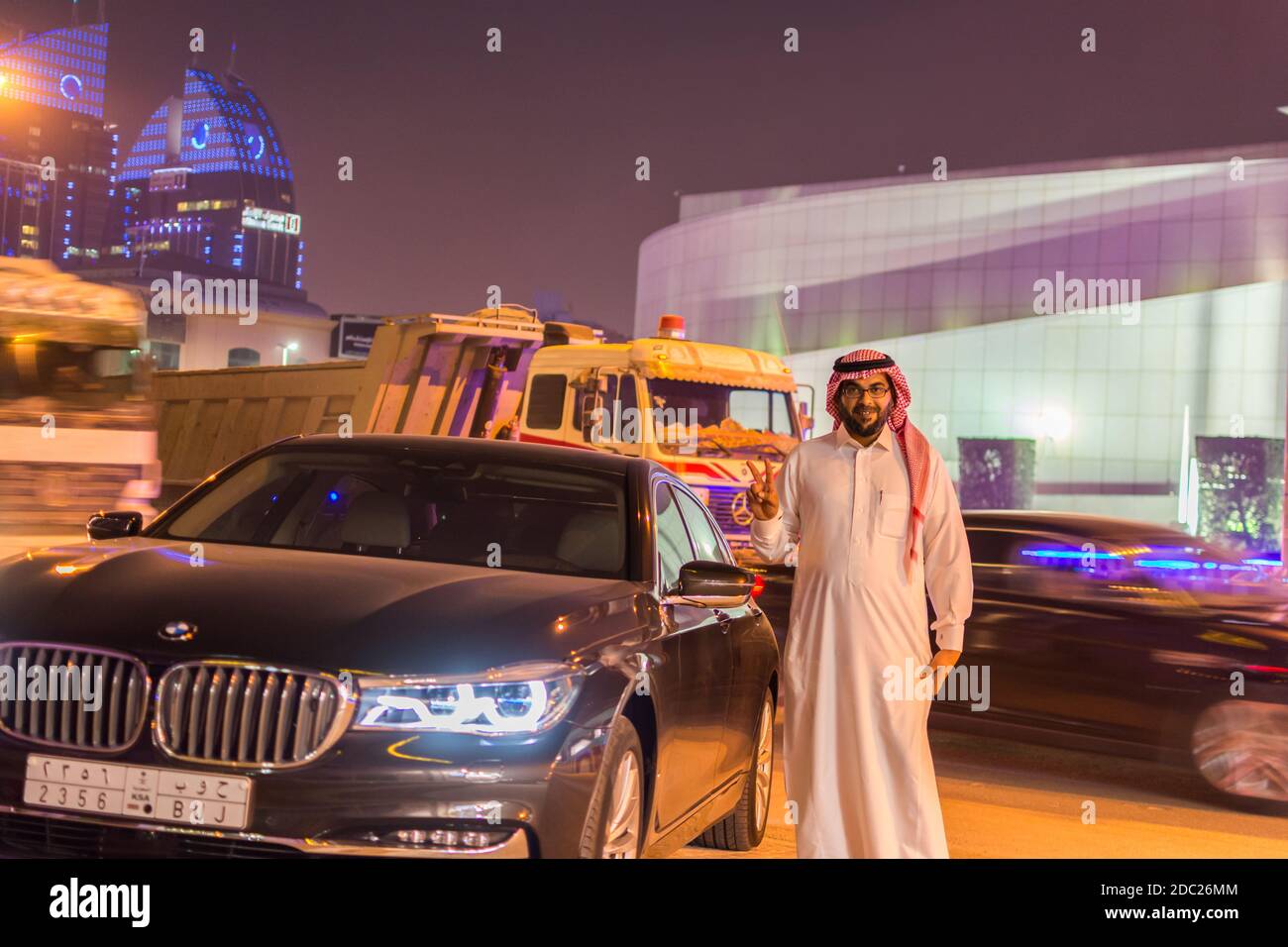 Ein reicher saudi-Araber, der traditionelle Kleidung trägt und neben einem Luxusauto in der Nacht im Olaya District von Riad, Saudi-Arabien steht Stockfoto