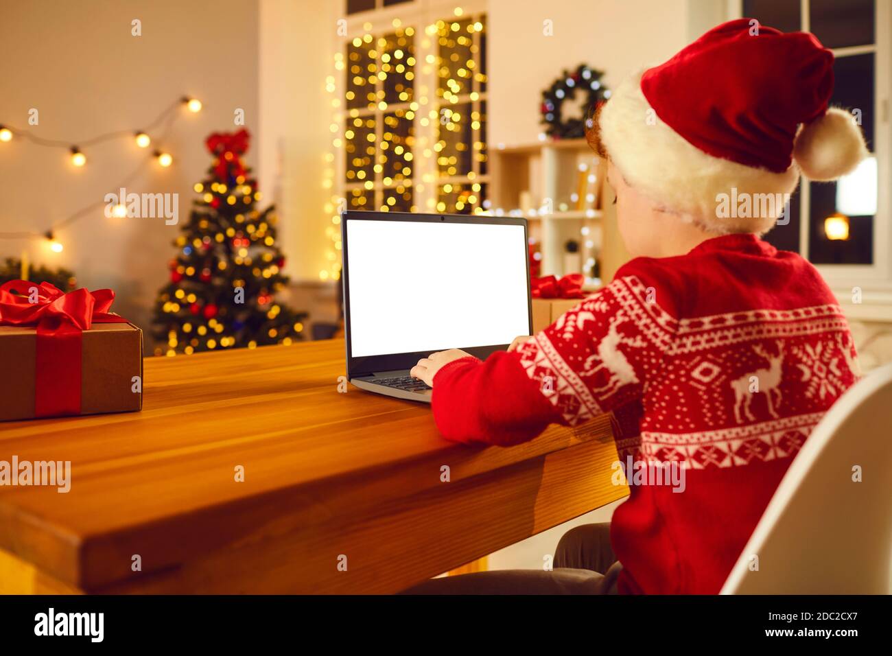 Junge im festlichen Weihnachtsmann Kostüm und Hut sitzen und tippen Weihnachten Gratulation oder chatten online auf dem Laptop Stockfoto