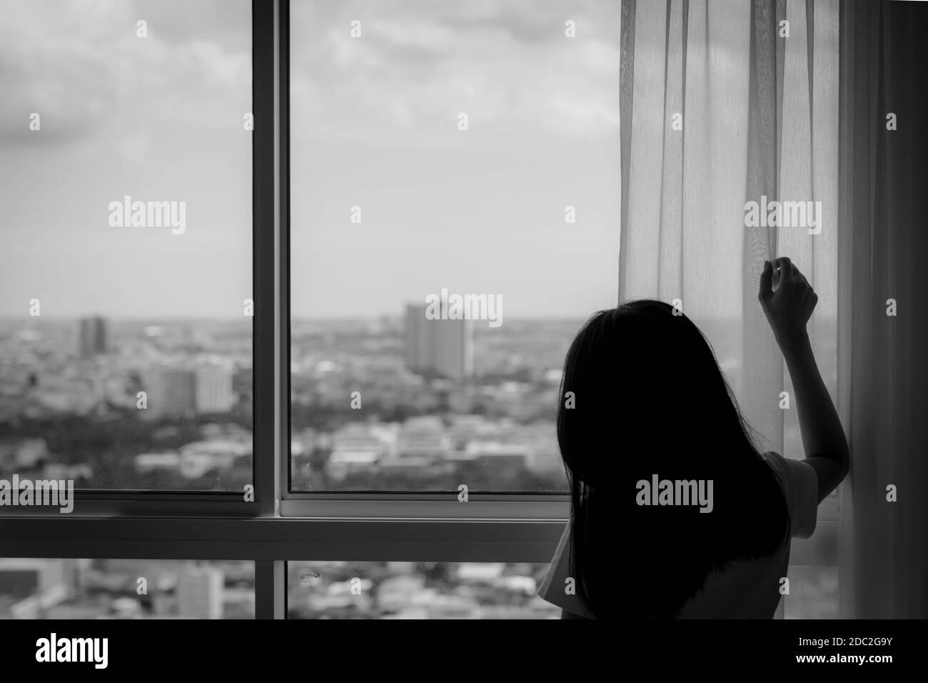 Rückansicht einer Frau, die den Vorhang hielt und aus dem Glasfenster schaute. Depressive Frau von der Sperre und Quarantäne von Coronavirus Pandemie. Mental er Stockfoto