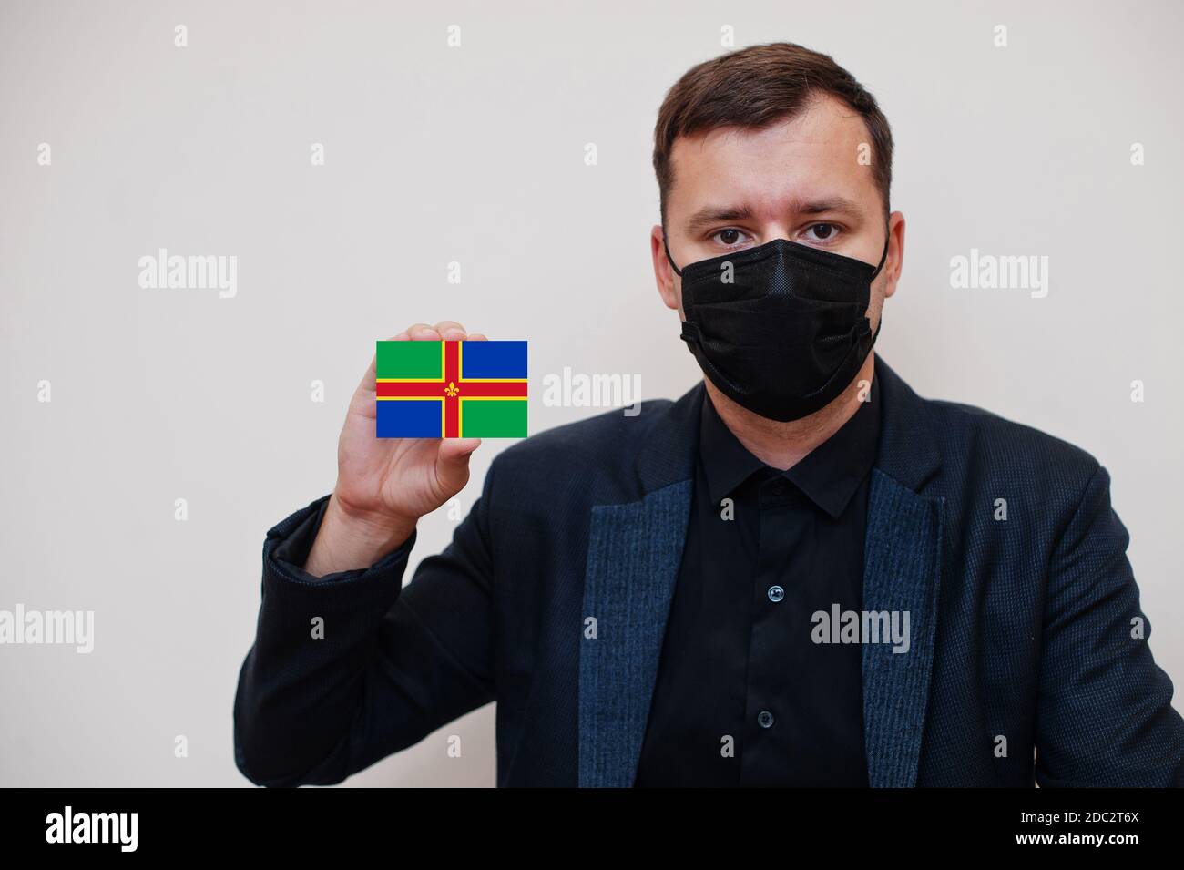 Mann tragen schwarz formell und schützen Gesichtsmaske, halten Lincolnshire Flagge Karte isoliert auf weißem Hintergrund. Vereinigtes Königreich Grafschaften England Coronavirus Stockfoto