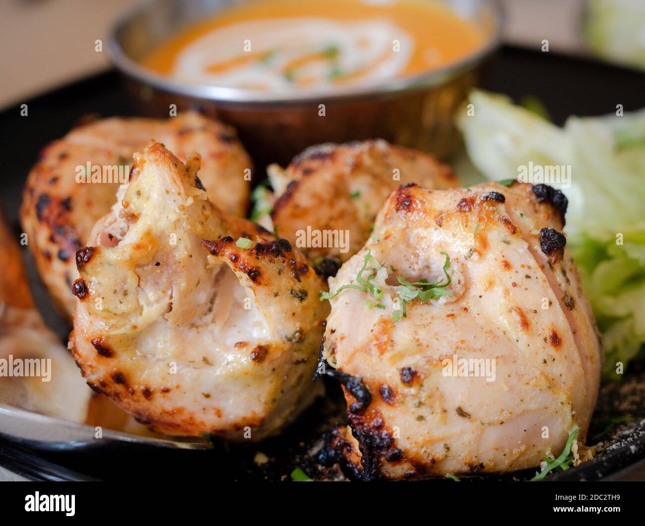 Marinierte Hähnchenstücke vor einer Schüssel mit Currysauce in einem indischen Restaurant in England. Stockfoto