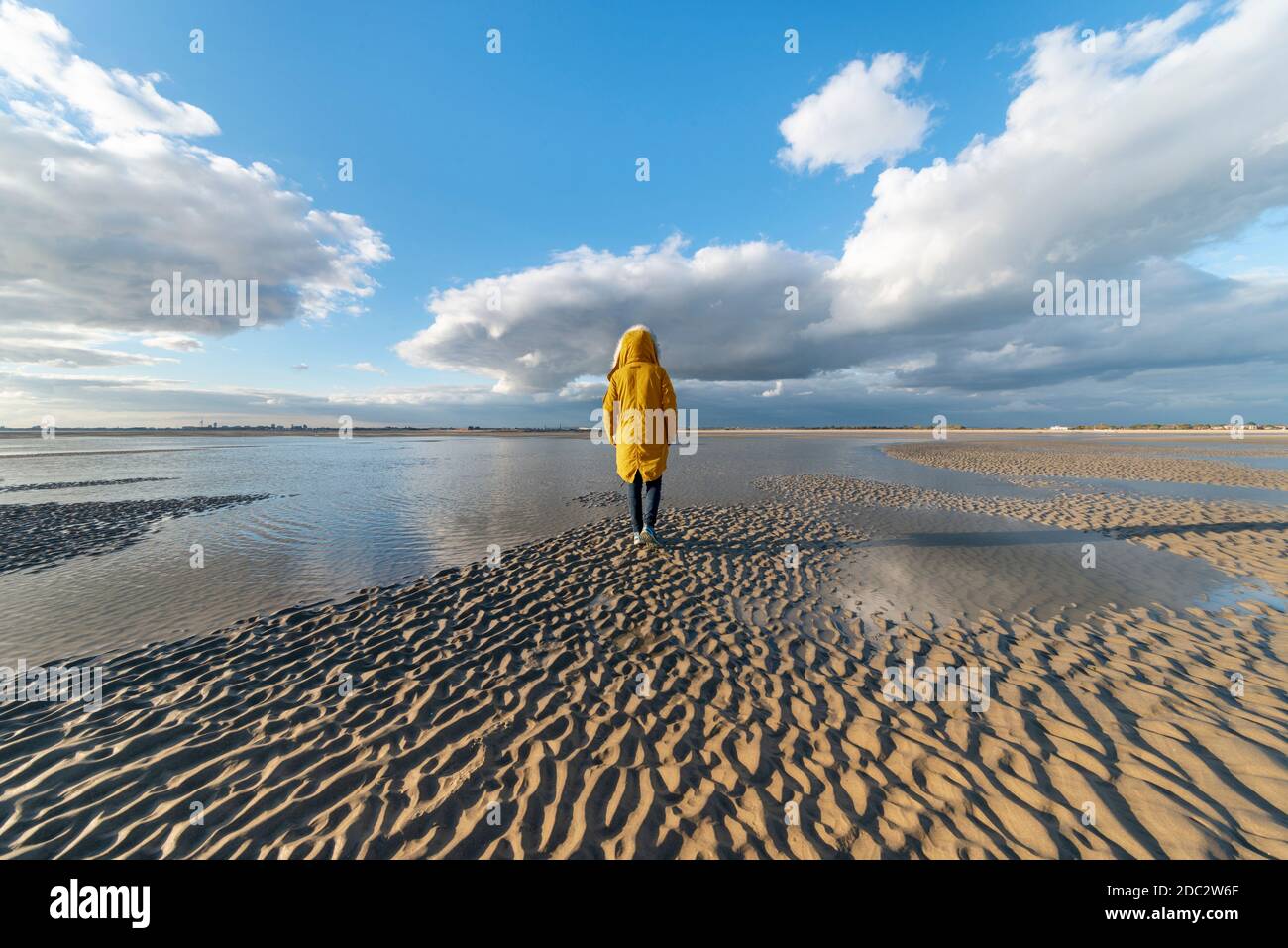 Strand bei Ebbe mit einer Person in einem gelben Mantel, Rückansicht. Stockfoto