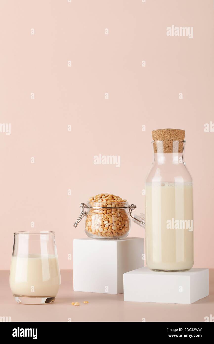 Erbsenmilch in der Flasche und Glas mit Erbsen im Glas auf weißem Sockel auf beigem Hintergrund. Glutenfreies, laktosefreies Produkt. Speicherplatz kopieren. Stockfoto