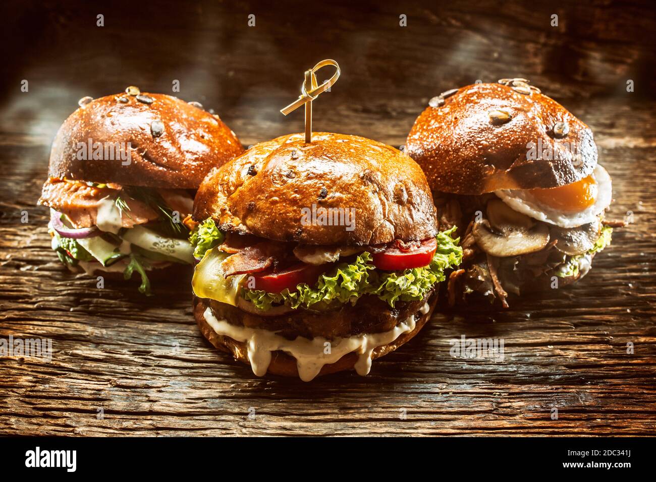 Vorderansicht auf drei große, Rindfleisch Lachs und Kebab Burger gefüllt mit frischem Gemüsesalat und Dressing Stockfoto