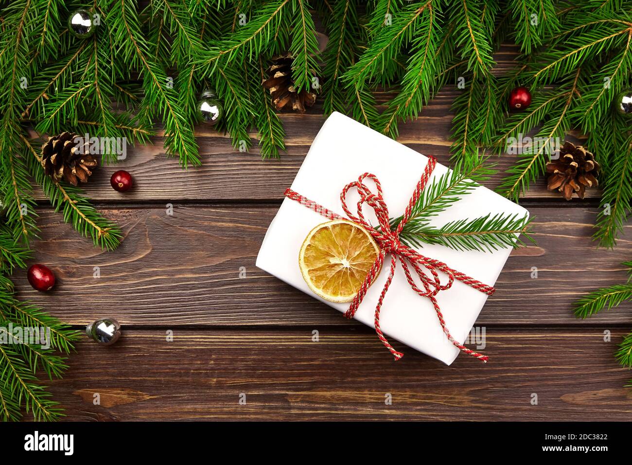 Schmückt weihnachts-Geschenkbox mit Tannenzweigen, Zapfen und roten Beeren auf Holztisch, Draufsicht. Weihnachtskomposition. Stockfoto