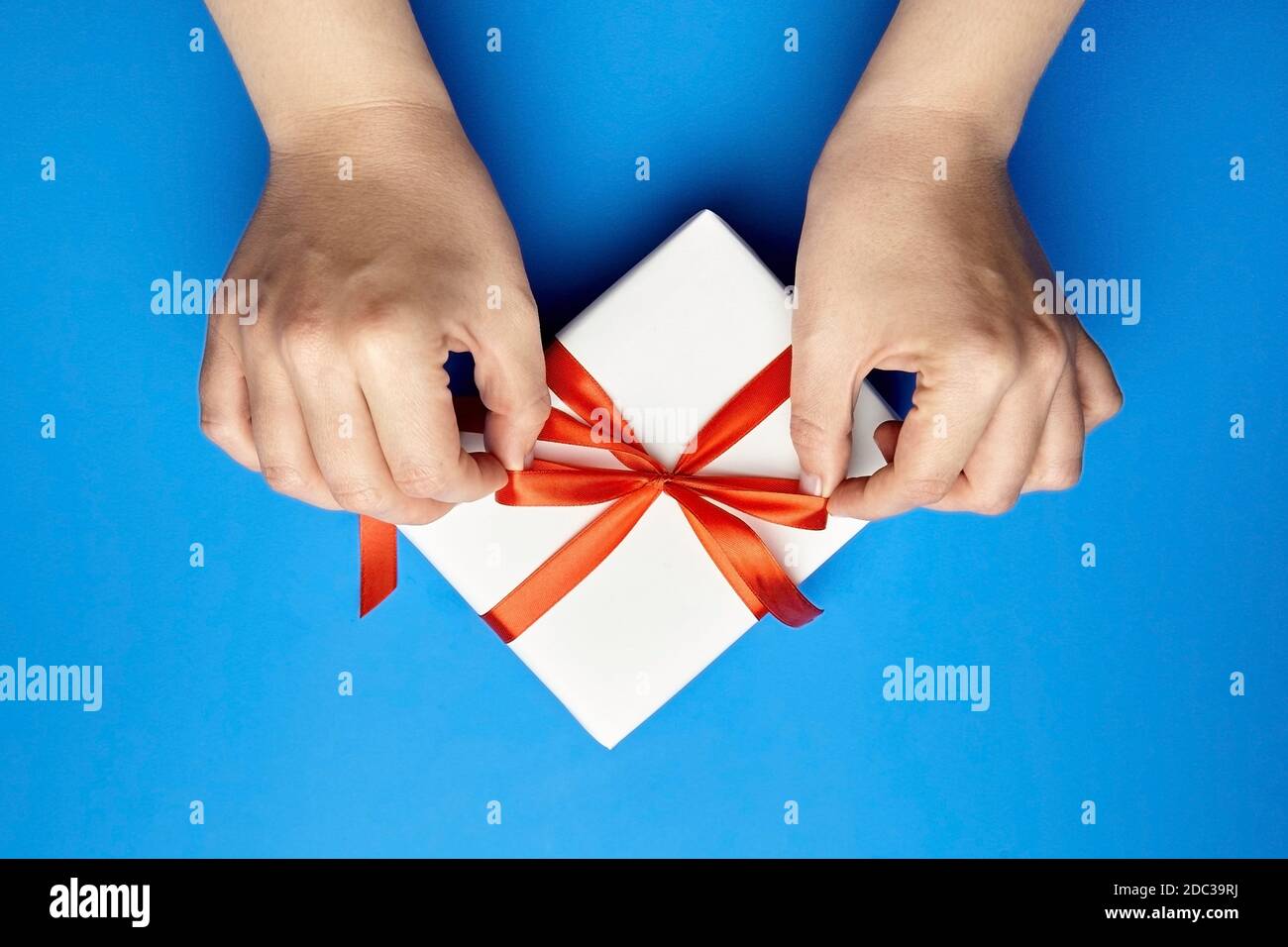 Hände binden roten Band auf weißen Geschenkbox auf blau Hintergrund Stockfoto