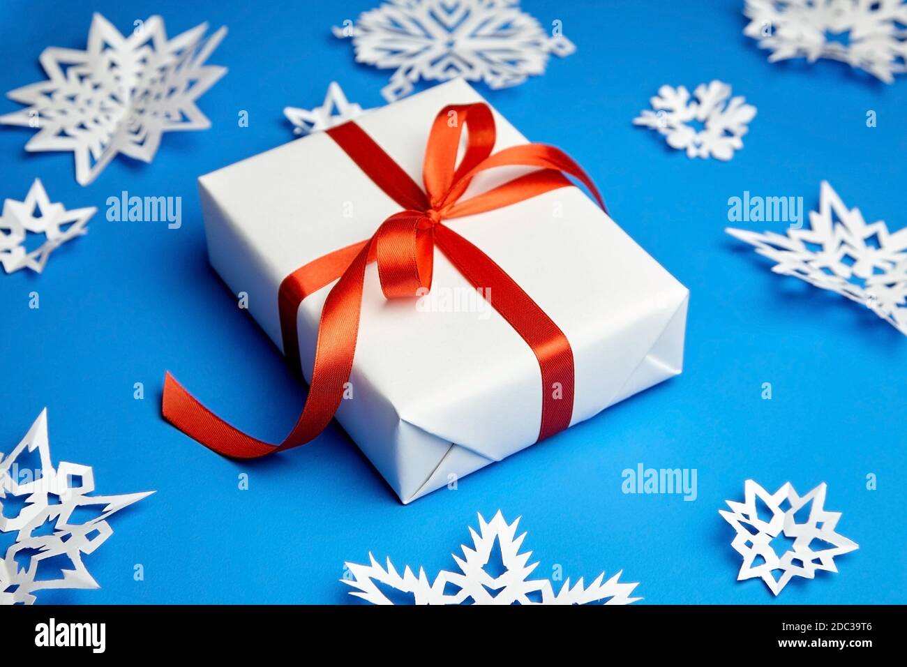 Weiße Geschenkbox mit rotem Band und Papier Schneeflocken auf Blau Stockfoto