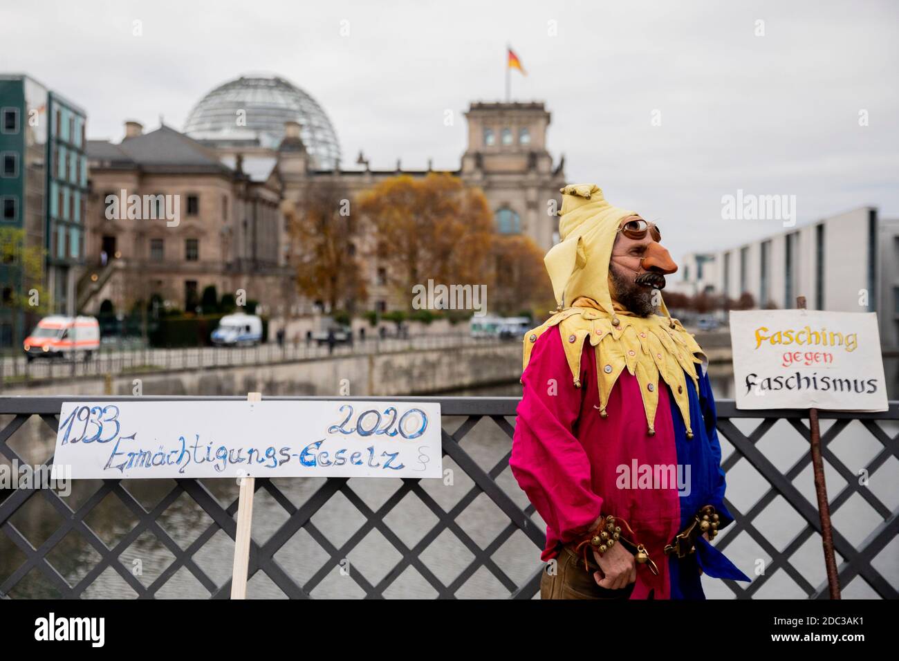 Berlin, Deutschland. November 2020. Ein als Narr verkleideter Mann steht bei einer Demonstration gegen die Corona-Beschränkungen der deutschen Regierung in der Nähe des Reichstagsgebäudes auf der Marshallbrücke. Neben ihm befinden sich Schilder mit den Aufsagen "1933 Enabling Act 2020" und "Fasching gegen Faschismus". Gleichzeitig soll die neue Fassung des Infektionsschutzgesetzes im Schnellverfahren durch Bundestag und Bundesrat gehen. Quelle: Christoph Soeder/dpa/Alamy Live News Stockfoto