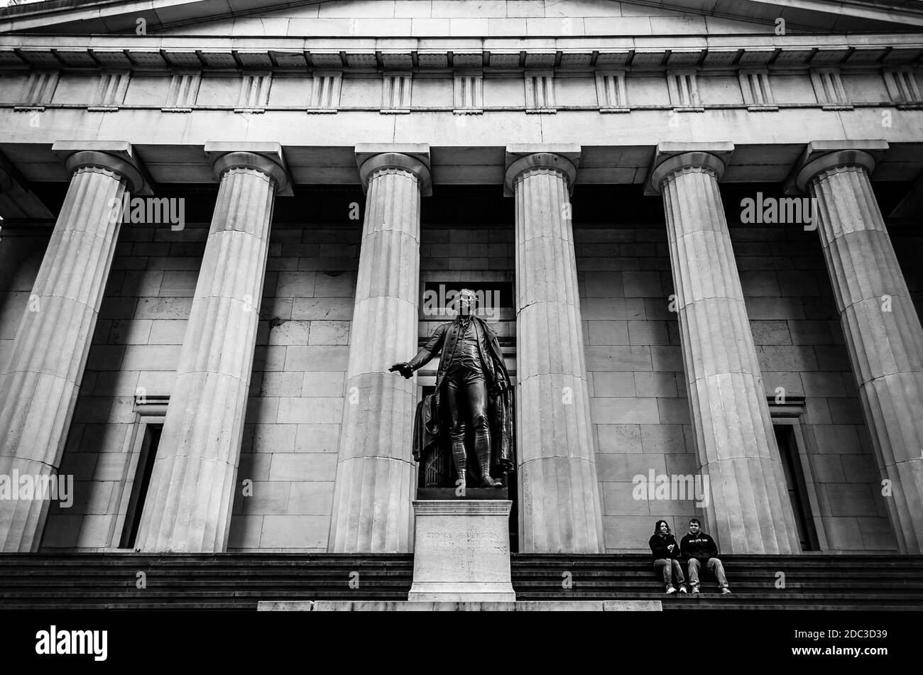 Schwarz-Weiß-Ansicht eines Paares, das vor dem Federal Building in der Wall Street sitzt. Gebäude im griechischen Stil im Finanzviertel, Manhattan, New York Stockfoto