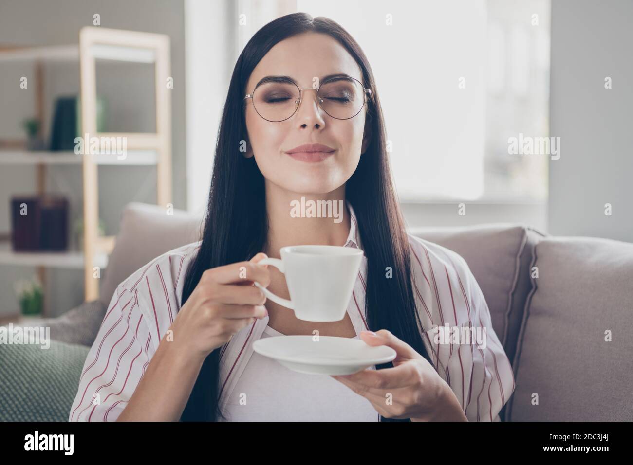 Portrait Foto von Brunette Frau trinken Kaffee riechende Aroma mit Geschlossene Augen halten Tasse zu Hause Stockfoto