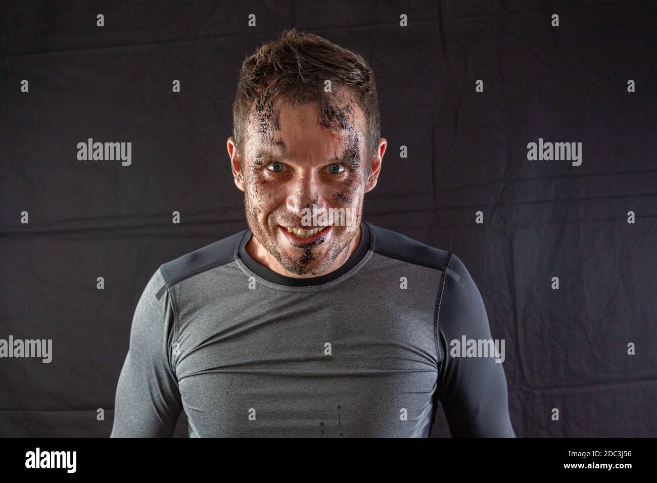 Schöner, gerackter Fitness-Mann in grauen Shorts, lächelnd und posiert vor dunkelschwarzem Hintergrund. Leichte Retuschierarbeit, Studiobeleuchtung. Stockfoto