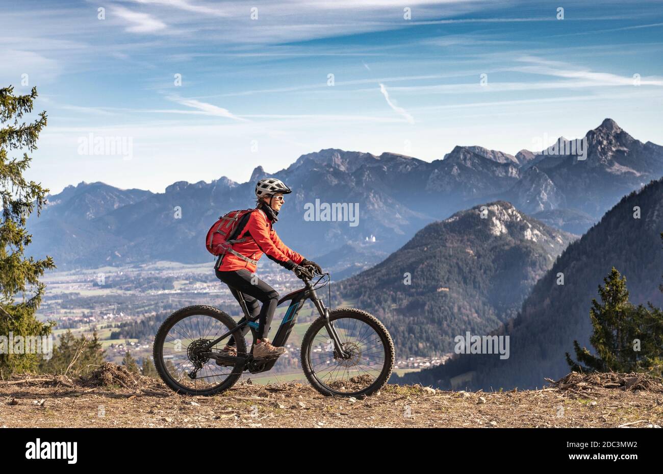 Hübsche ältere Frau, die ihr E-Mountainbike in den Bergen des Ostallgäus an warmen Herbsttagen mit dem Zugspitze im Hintergrund fährt Stockfoto