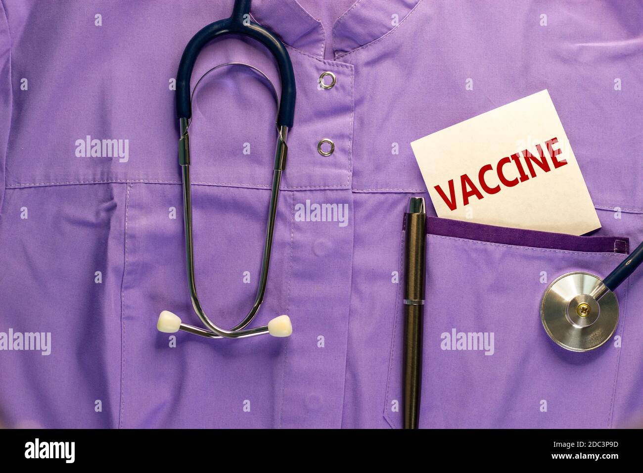 Medizinische Uniform, weiße Karte mit den Worten „Impfstoff“, Metallstift und Stethoskop. Medizinisches und covid-19 Pandemiekonzept. Stockfoto