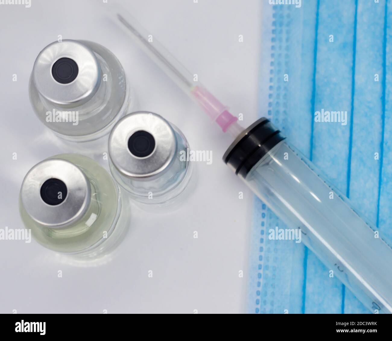 Impfstofffläschchen, Spritze und blaue medizinische Gesichtsmaske Stockfoto