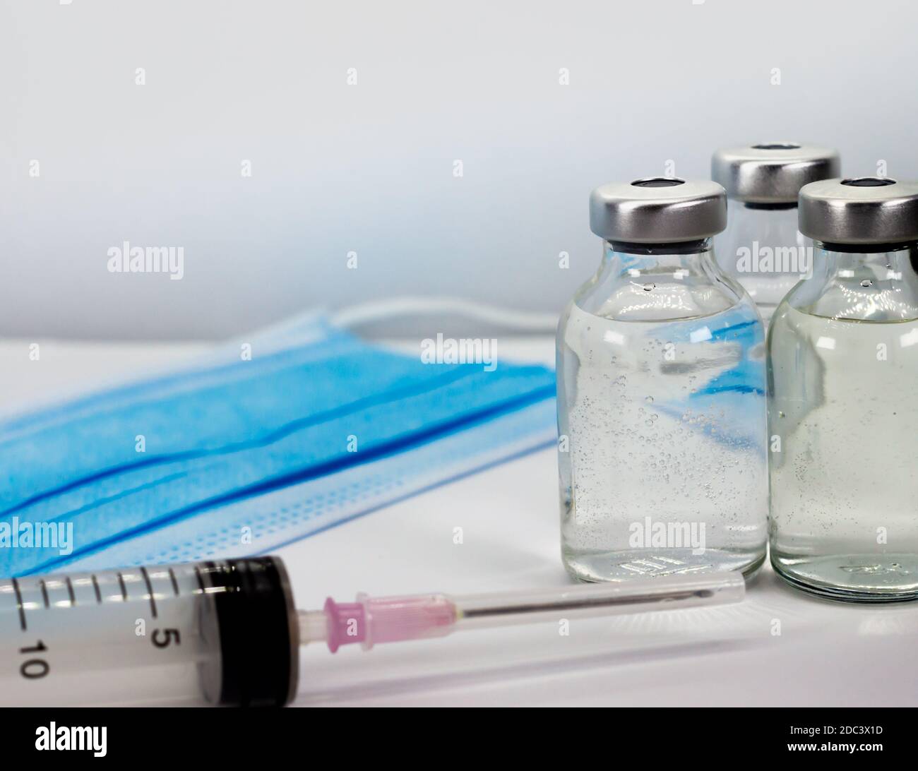 Impfstofffläschchen, Spritze und blaue medizinische Gesichtsmaske Stockfoto