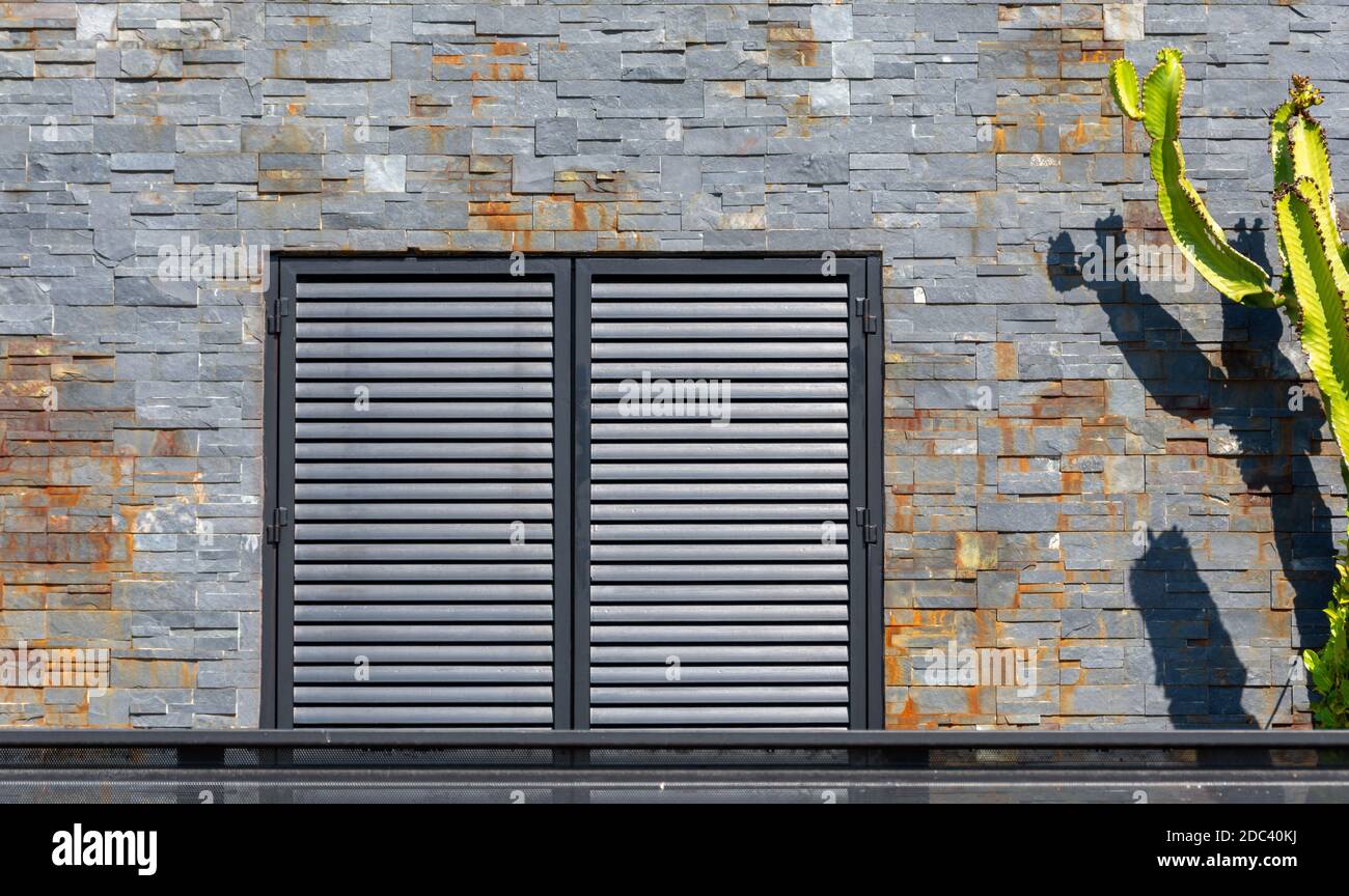 Ziegelfassade mit Fenster mit Metallläden und eine große Grüner Kaktus auf einer Seite Stockfoto