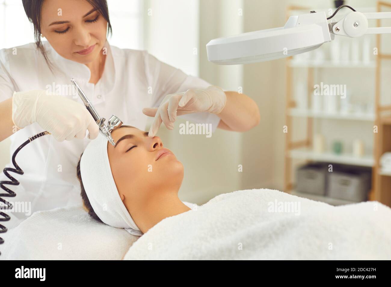 Lächelnder Dermatologe macht Verfahren der Gesichts-Sauerstoff-Therapie für junge Frau Stockfoto