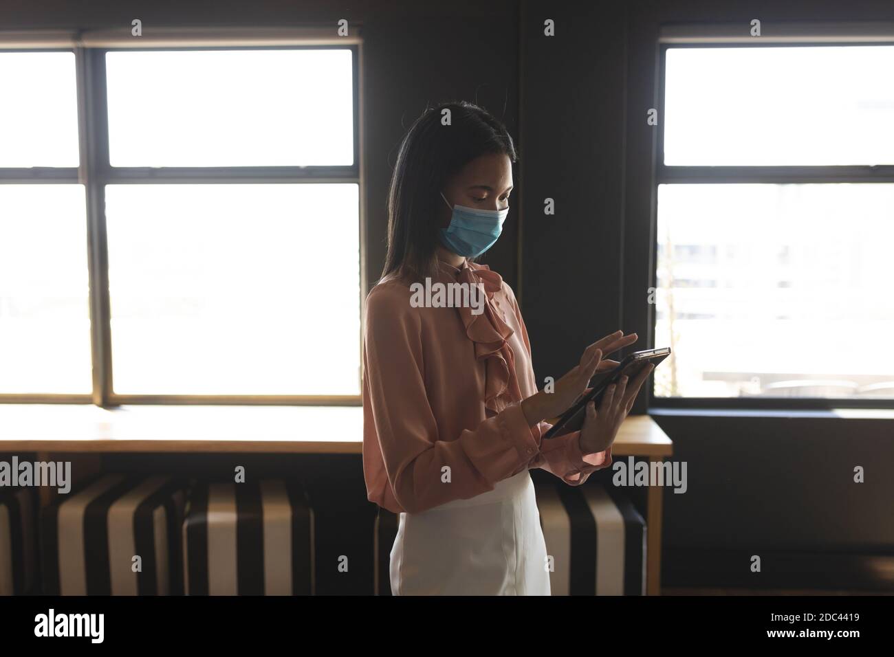 Asiatische Frau trägt Gesichtsmaske mit digitalen Tablet auf moderne Büro Stockfoto