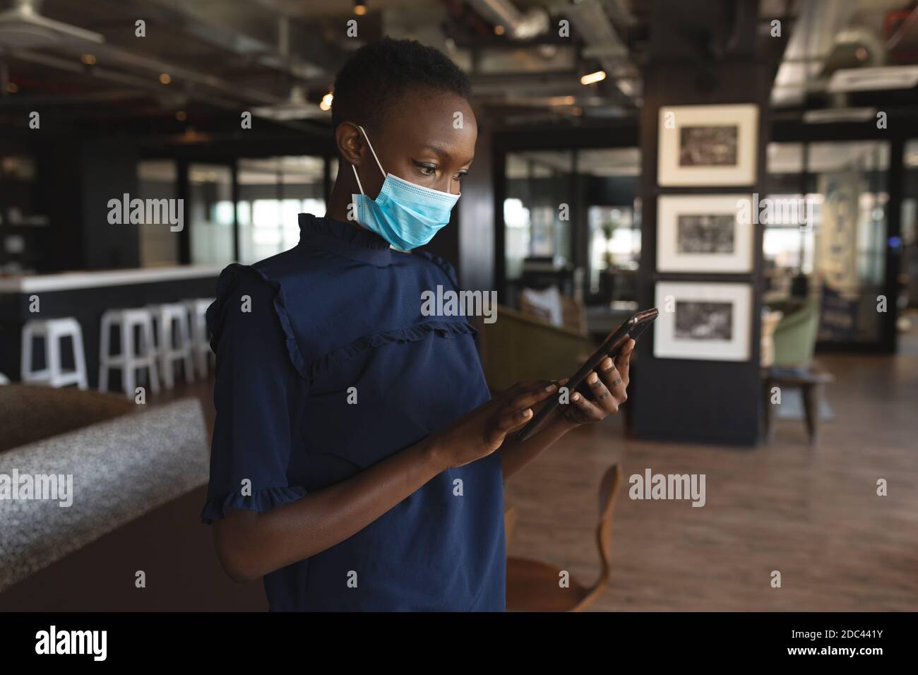 afroamerikanische Frau trägt Gesichtsmaske mit digitalen Tablet an Modernes Büro Stockfoto