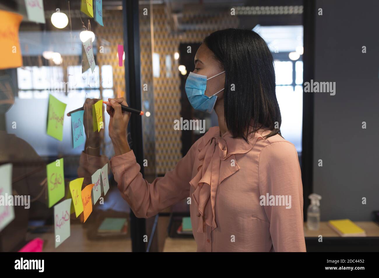 Asiatische Frau trägt Gesichtsmaske schreiben mit Marker Stift auf Glasplatine im modernen Büro Stockfoto