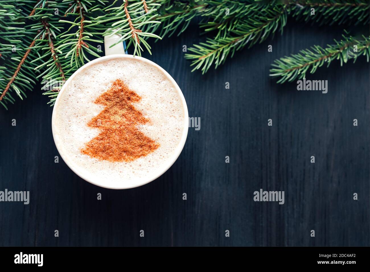 Draufsicht auf eine Tasse Cappuccino mit Milchschaum und Kakaokraft. Latte Art. Dunkler Holzhintergrund und Tannenbaum Stockfoto