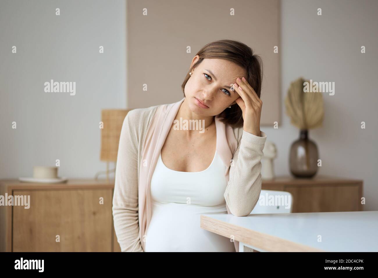 Schwangere Frau, die an Kopfschmerzen leidet, während sie am Tisch sitzt Stockfoto