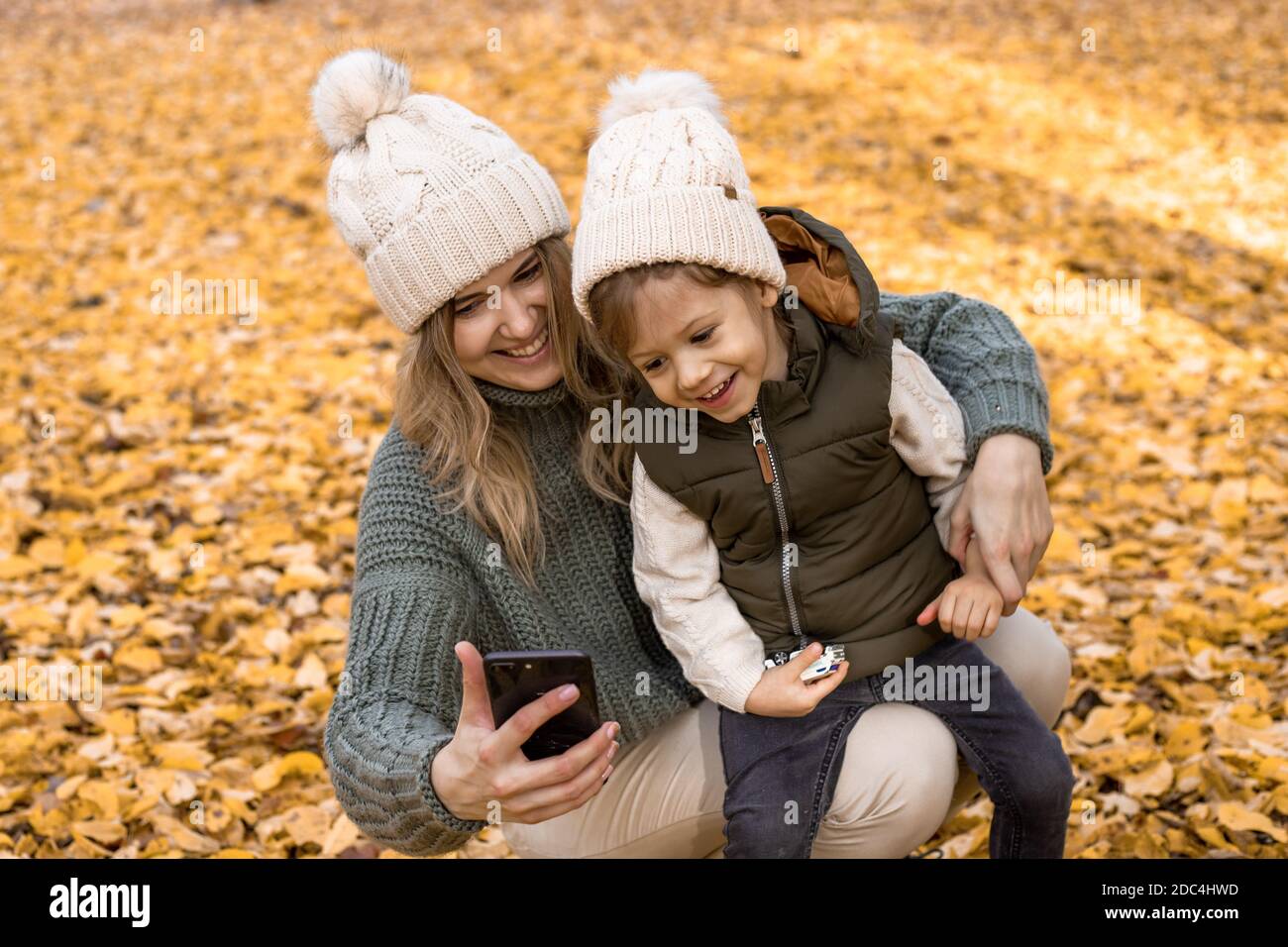 Fotos von glücklicher und lächelnder Mutter. Mutter mit kleinem Sohn in einem Herbstpark inmitten gelber Laubbäume machen ein Selfie oder nehmen eine Videobotschaft für Familie und auf Stockfoto