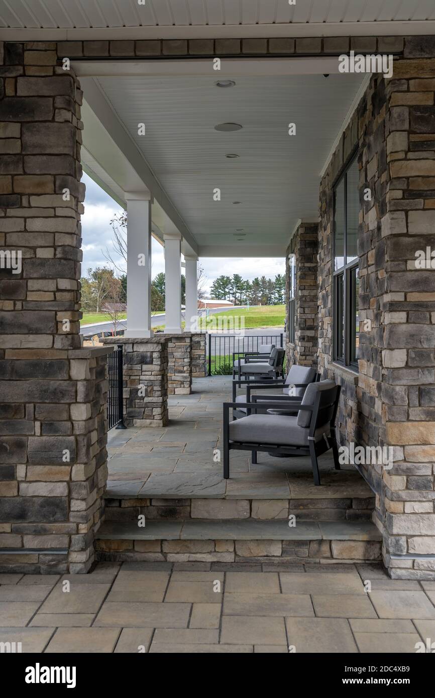 Überdachte Veranda mit furnierten weißen Säulen, Stühlen und Gartenmöbeln Stockfoto