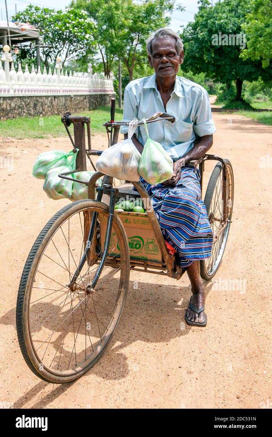 Ein körperlich behinderter Mann, der auf dem Heimweg ein modifiziertes Fahrrad fährt, nachdem er Obst auf einem lokalen Markt in Sigiriya in Zentral-Sri Lanka gekauft hat. Stockfoto