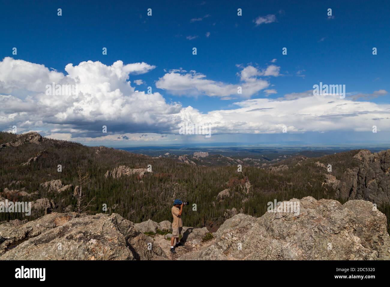 Ein Fotograf steht auf einer Granitfelsen-Formation und fotografiert mit einem dynamischen Landschaftshintergrund im Custer State Park, South Dakota. Stockfoto