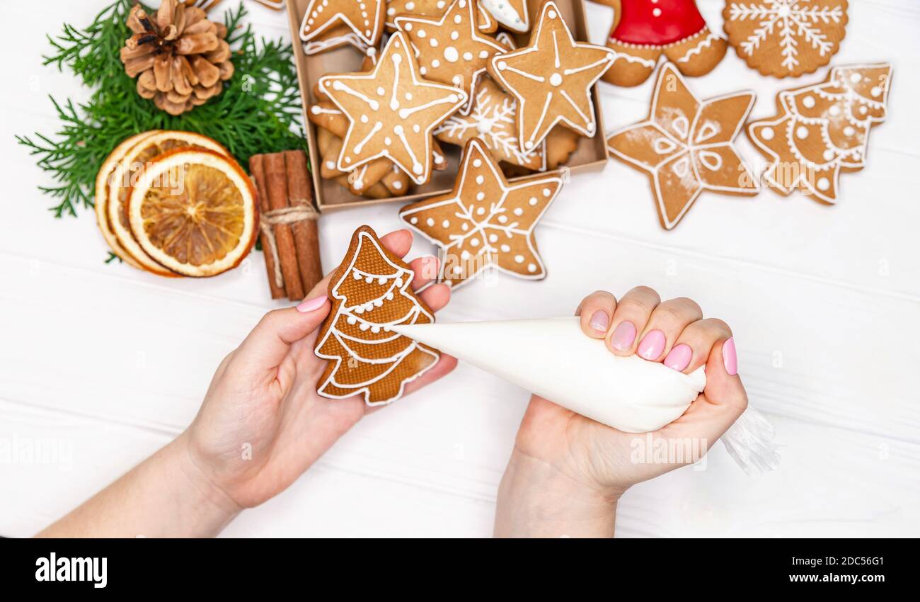 Weibliche Hände malen Weihnachts Lebkuchenkuchen. Feiertagsbäcken Stockfoto