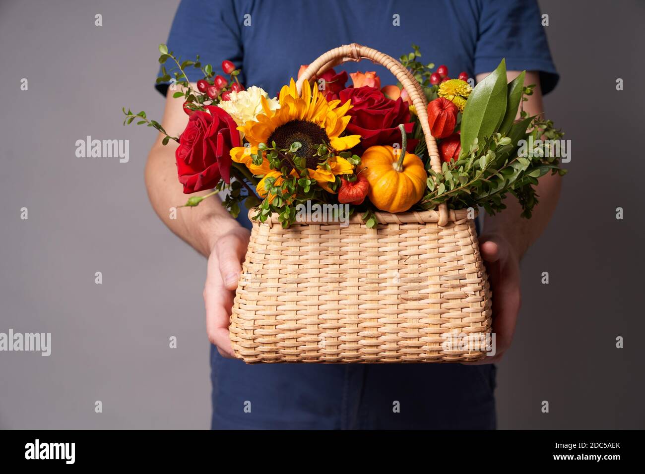 Ein weißer Mann in einem blauen T-Shirt hält einen Blumenkorb mit einem Kopierplatz auf einem grauen Hintergrund, Blumen Lieferung Stockfoto