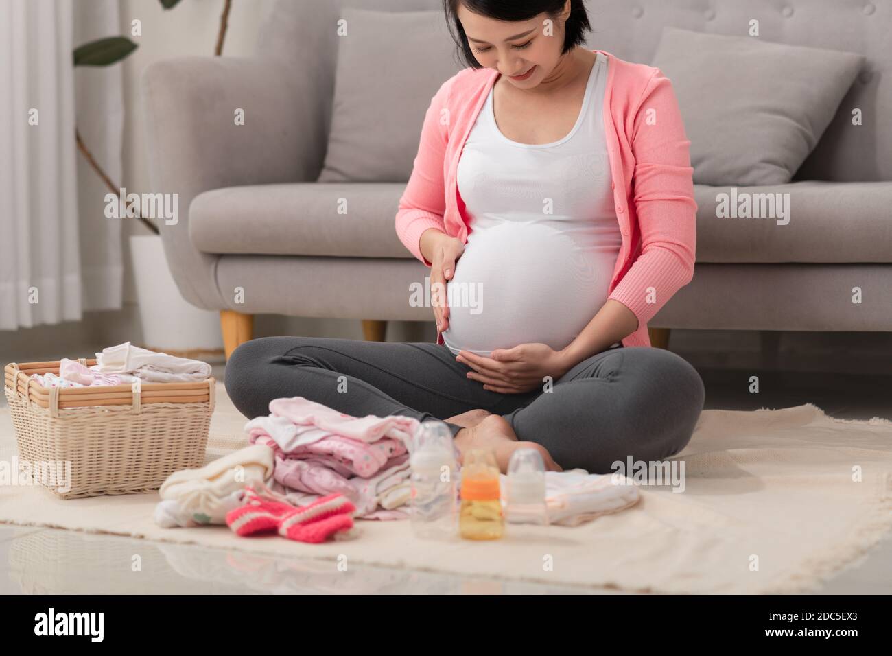 Eine glückliche schwangere Frau, die eine Liste der Dinge für ihr ungeborenes Baby zu Hause auf dem Boden überprüft Stockfoto