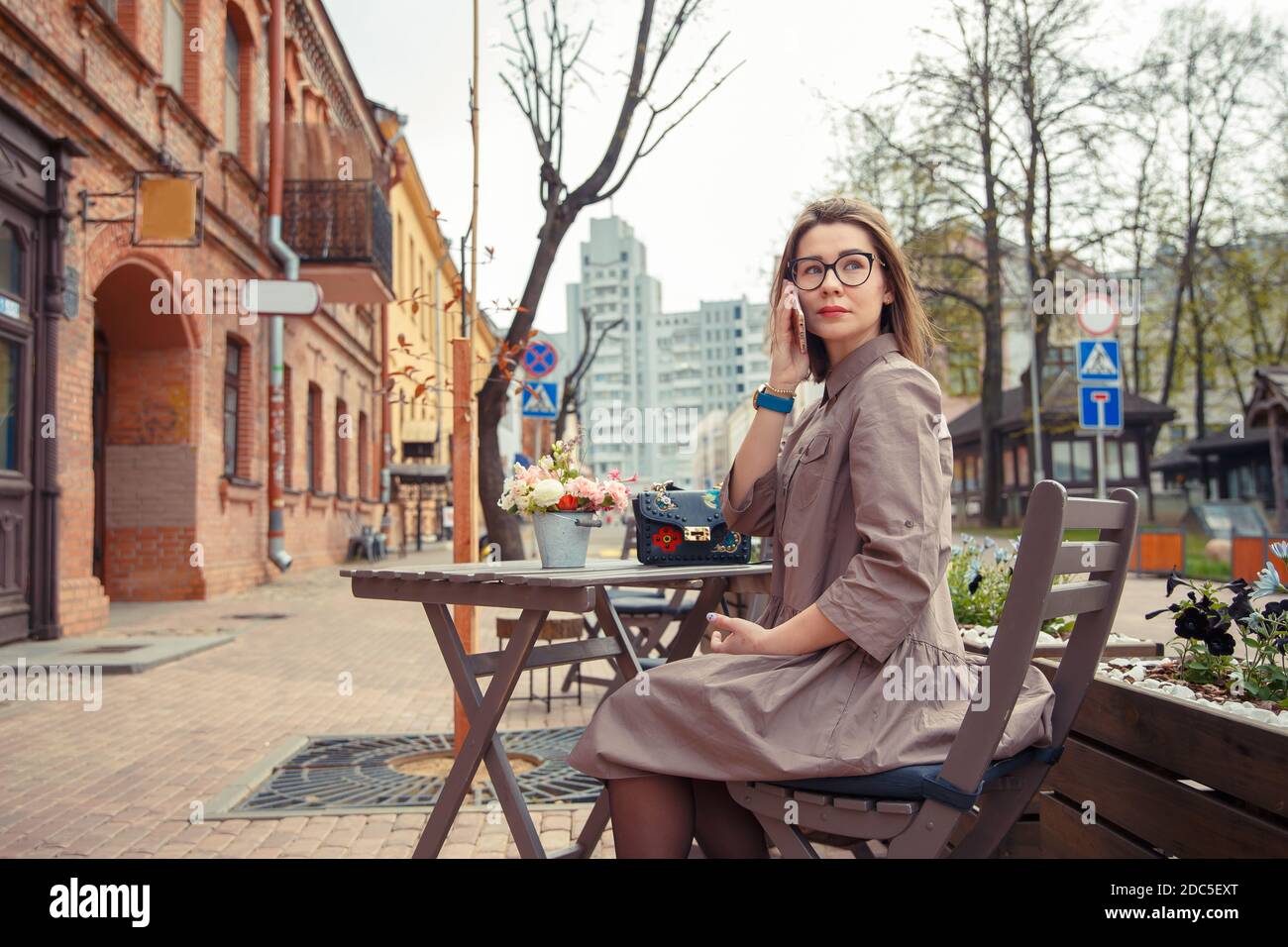 Schöne Frau Reisende auf der Straße der Altstadt. Geschäftsfrau sitzt an einem Tisch in einem Sommercafé und spricht am Telefon Stockfoto