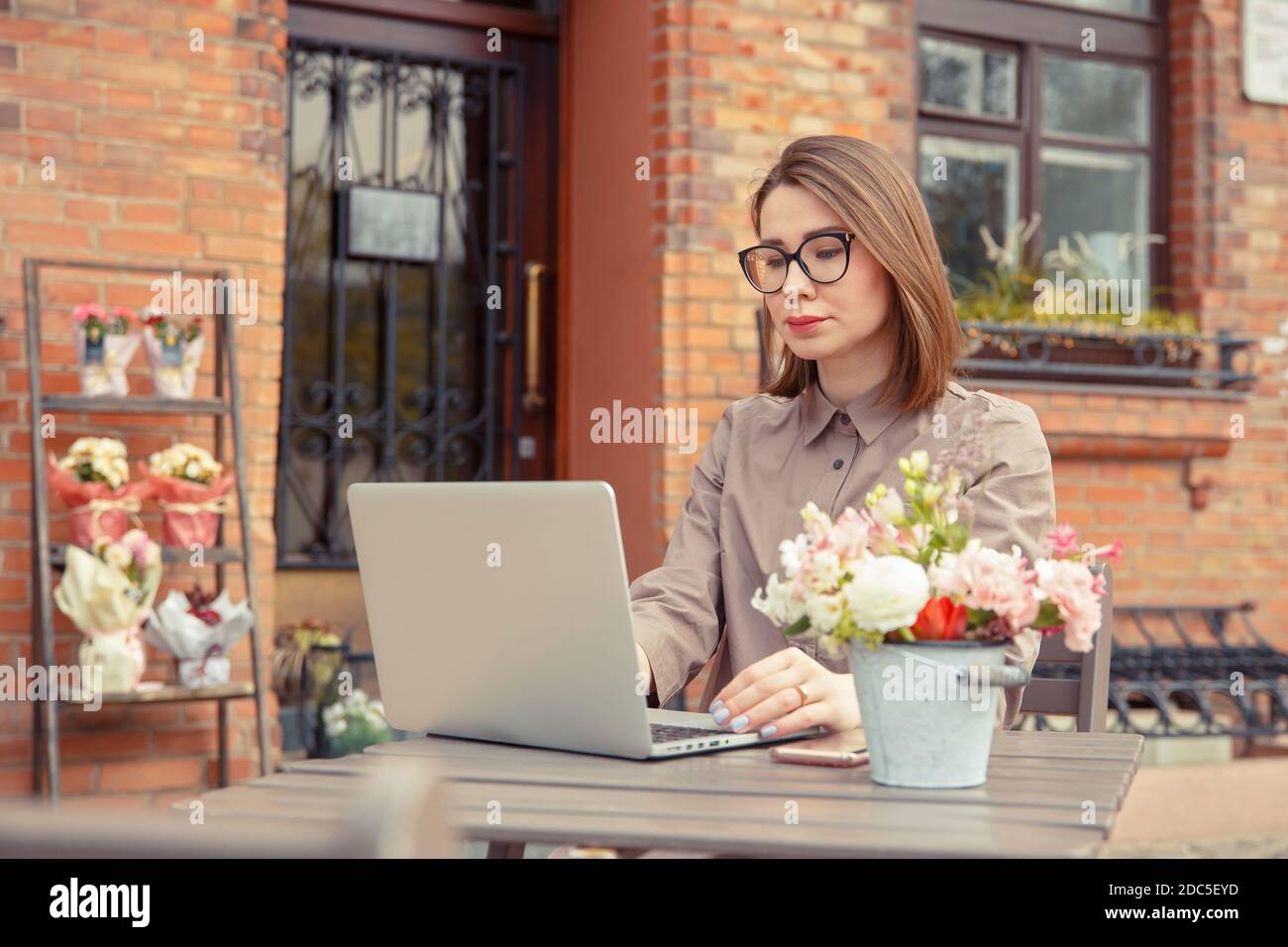 Schöne Frau Reisende auf der Straße der Altstadt. Geschäftsfrau sitzt an einem Tisch in einem Sommercafé und arbeitet an einem Computer Stockfoto