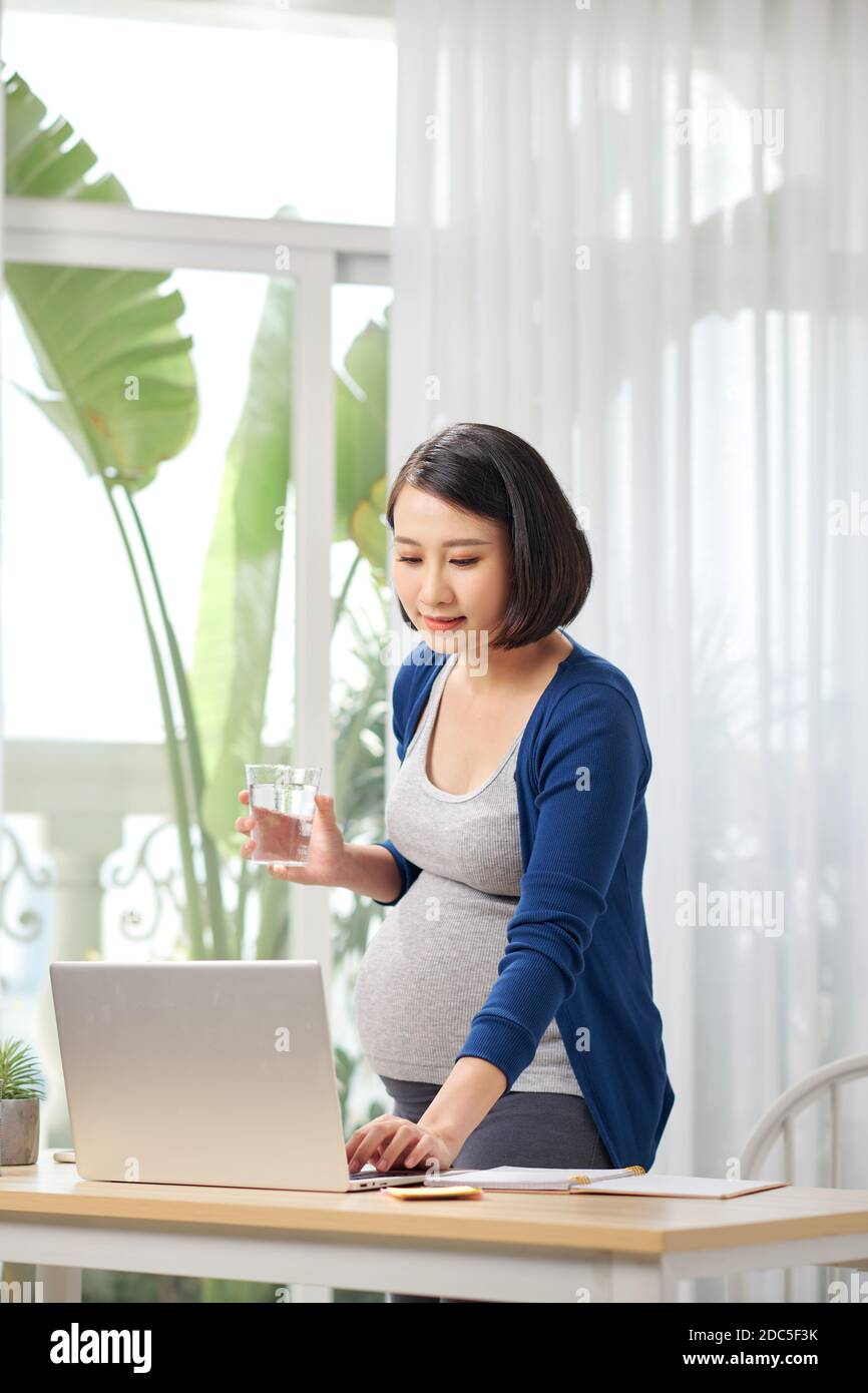 Schwangere Frau im Home Office in der Nähe von Tisch mit Computer und Trinkwasser Stockfoto