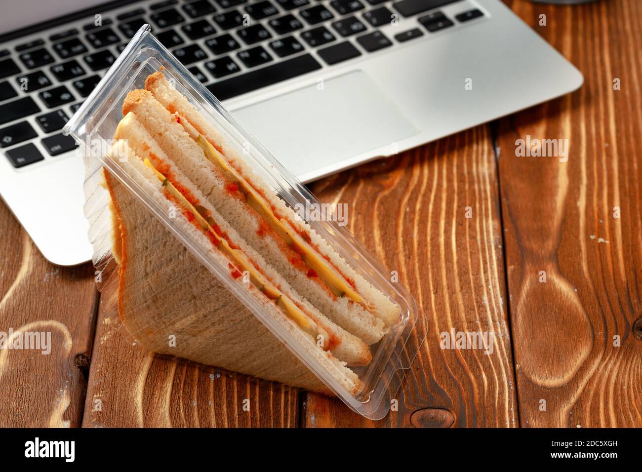 Gepacktes Sandwich und offener Laptop auf braunem Holztisch Stockfoto