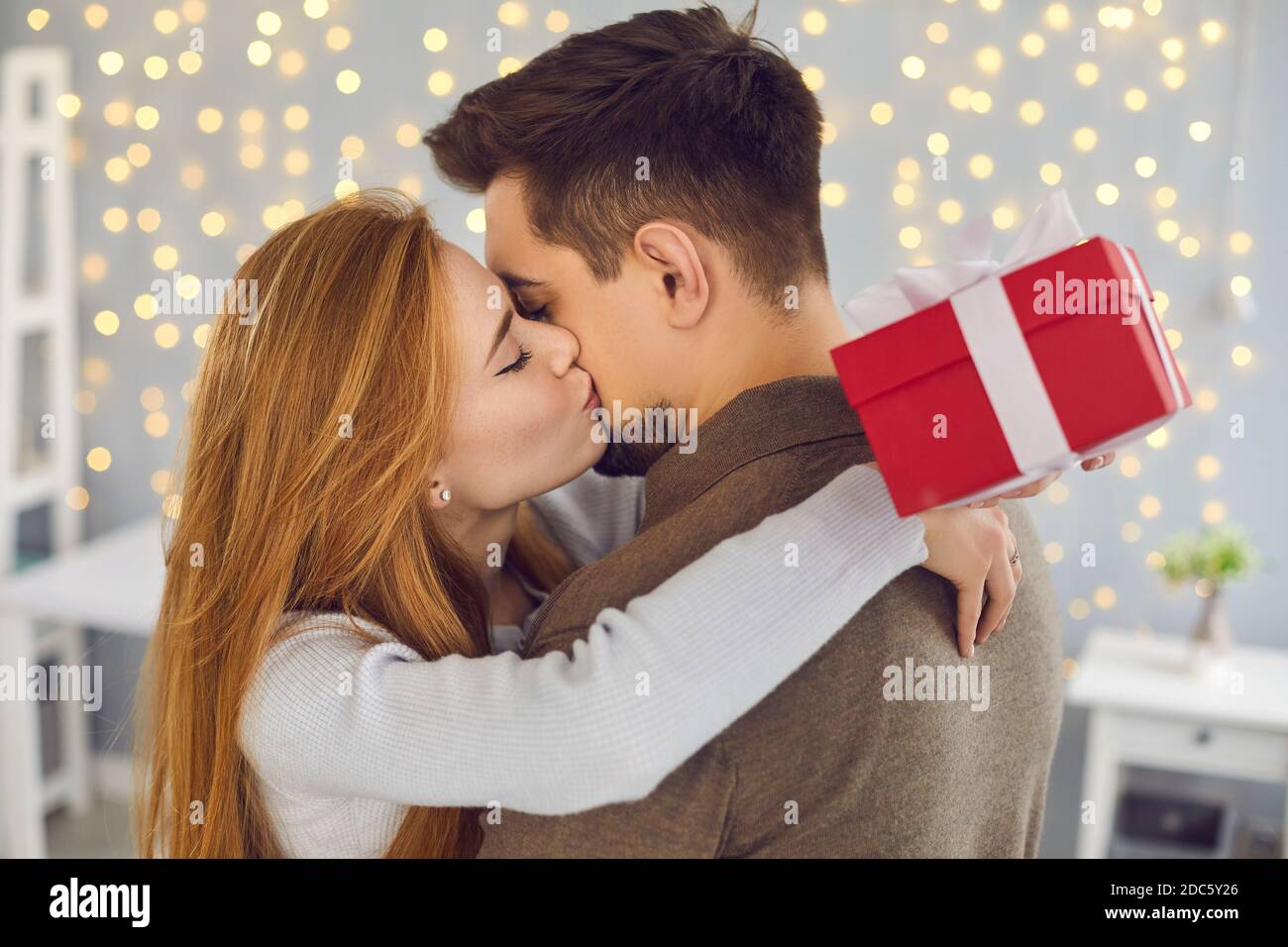 Seitenansicht einer schönen jungen Frau, die ihren Mann in Dankbarkeit für ein Geschenk auf die Wange küsst. Stockfoto