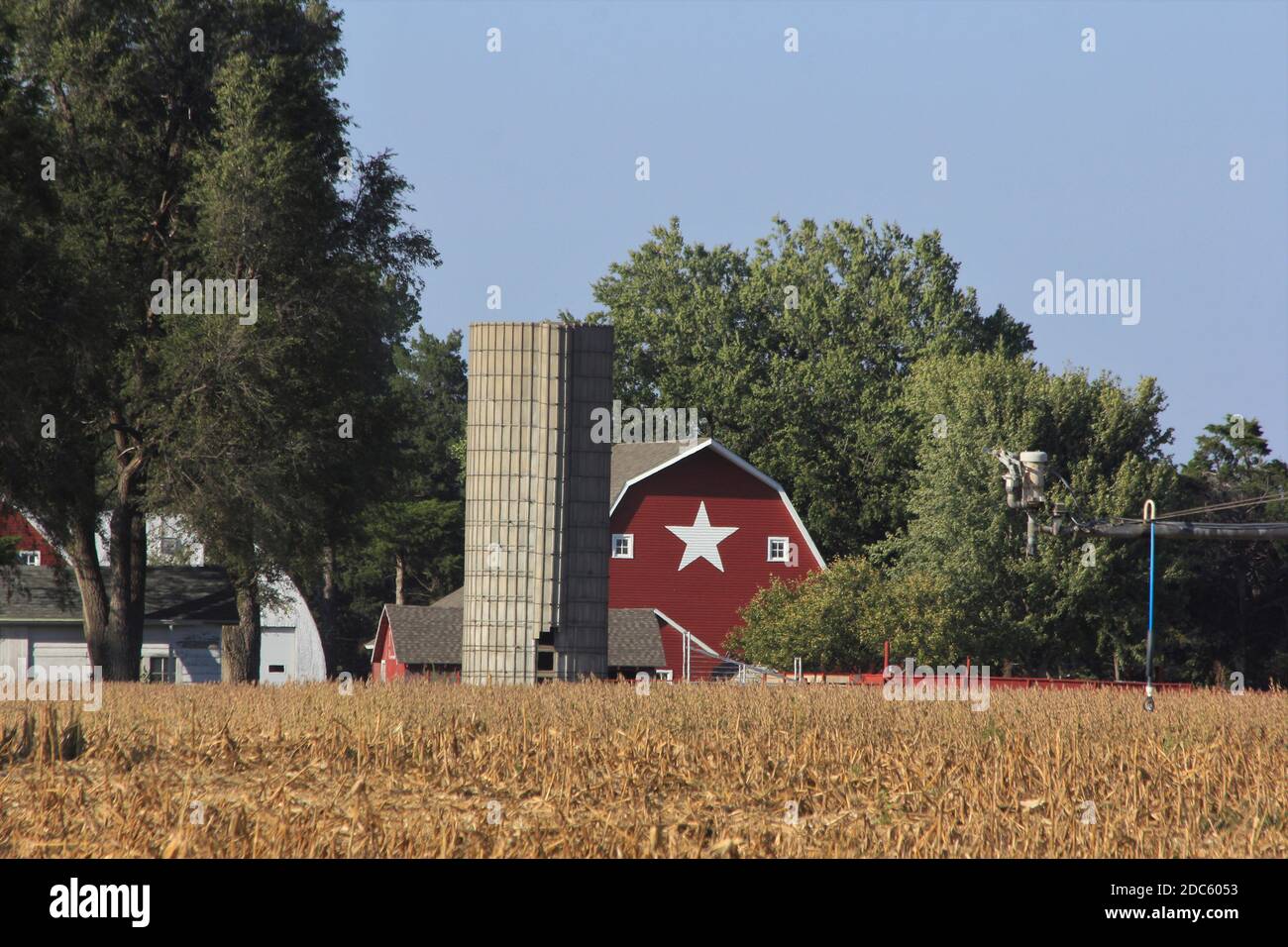Kansas Red Barn mit blauem Himmel, Bäumen und einem weißen Stern auf der Scheune mit einem Silo draußen im Land. Stockfoto