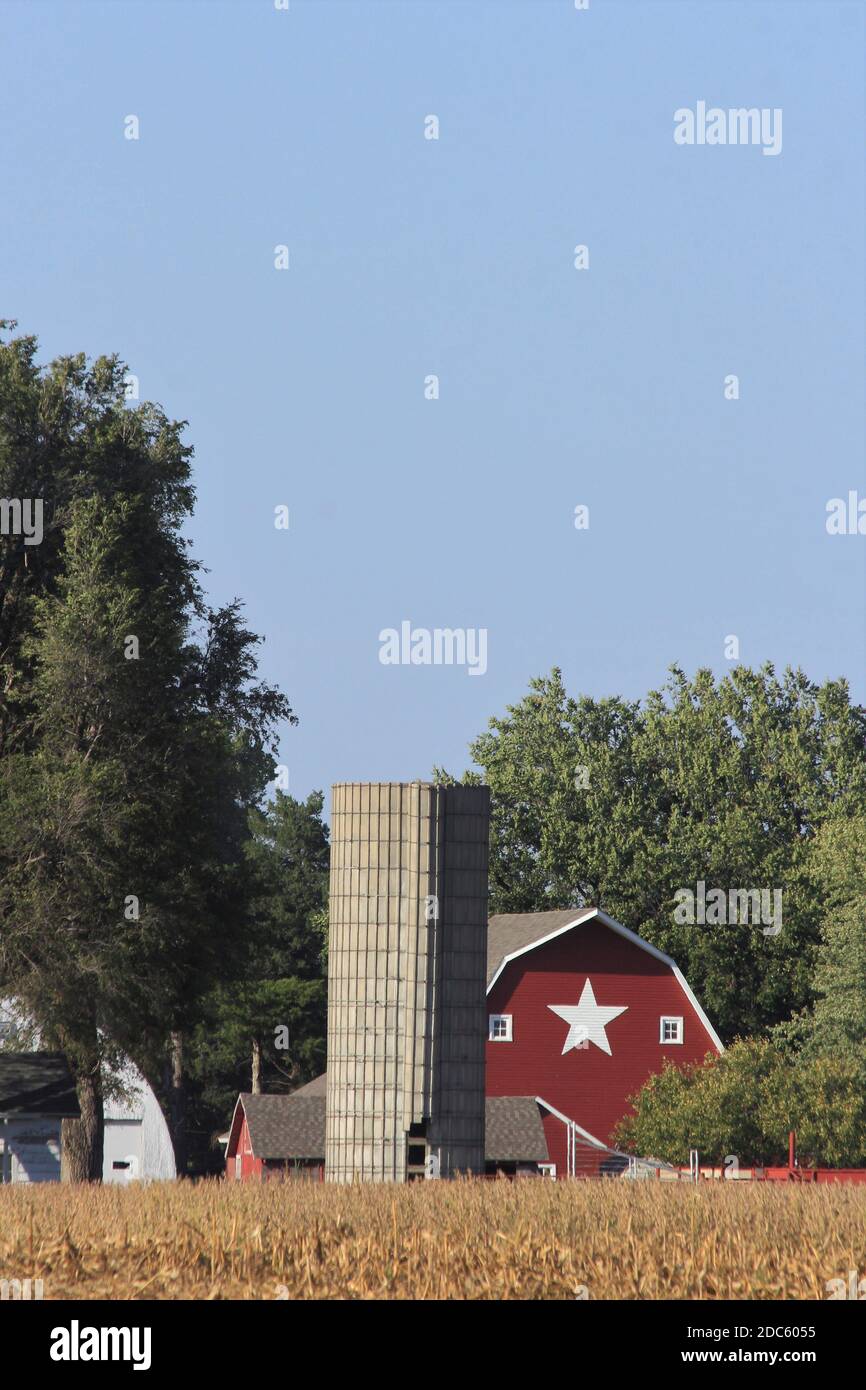 Kansas Red Barn mit blauem Himmel, Bäumen und einem weißen Stern auf der Scheune mit einem Silo draußen im Land. Stockfoto