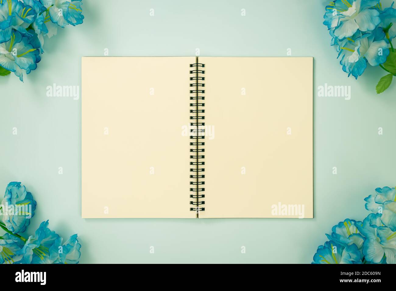 Tischchen Spiral Notizbuch oder Feder Notizbuch Mockup in ungefüttert Tippen Sie auf Mittelrahmen und blaue Blumen an der Ecke ein Blau Pastell minimalistischen Hintergrund in Stockfoto