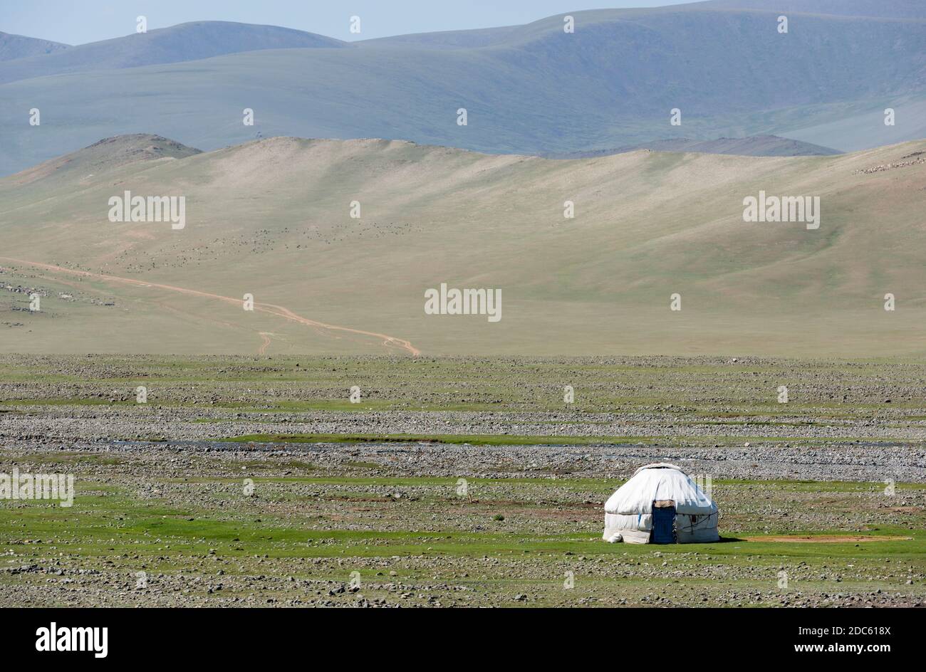 Jurte in einem Tal auf der Steppe der Mongolei mit einer Herde von Ziegen und Schafen im Hintergrund auf dem Hügel. Stockfoto