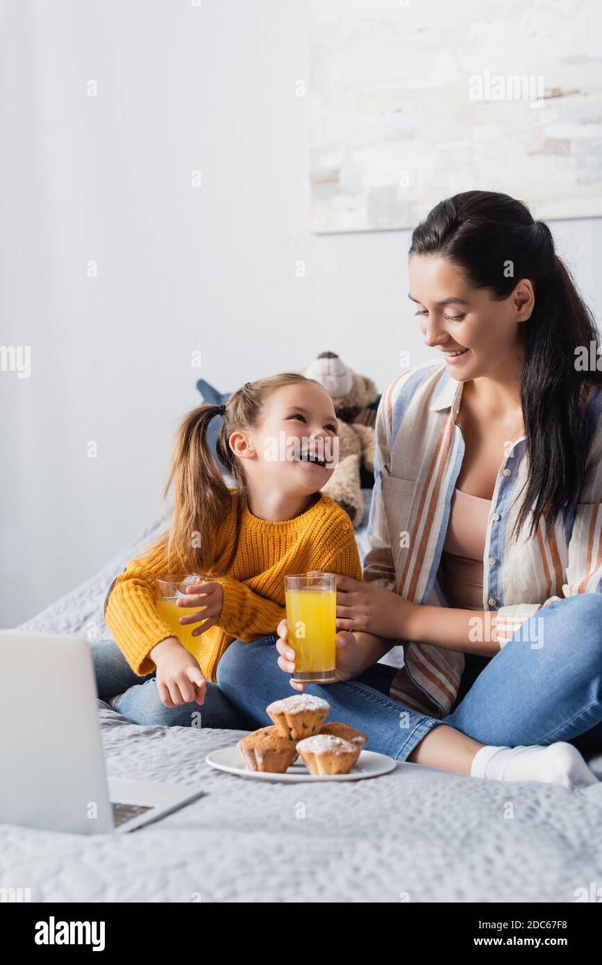 Glückliche Mutter und Tochter, die einander beim Halten anguckend Orangensaft und Filme auf dem Laptop ansehen Stockfoto