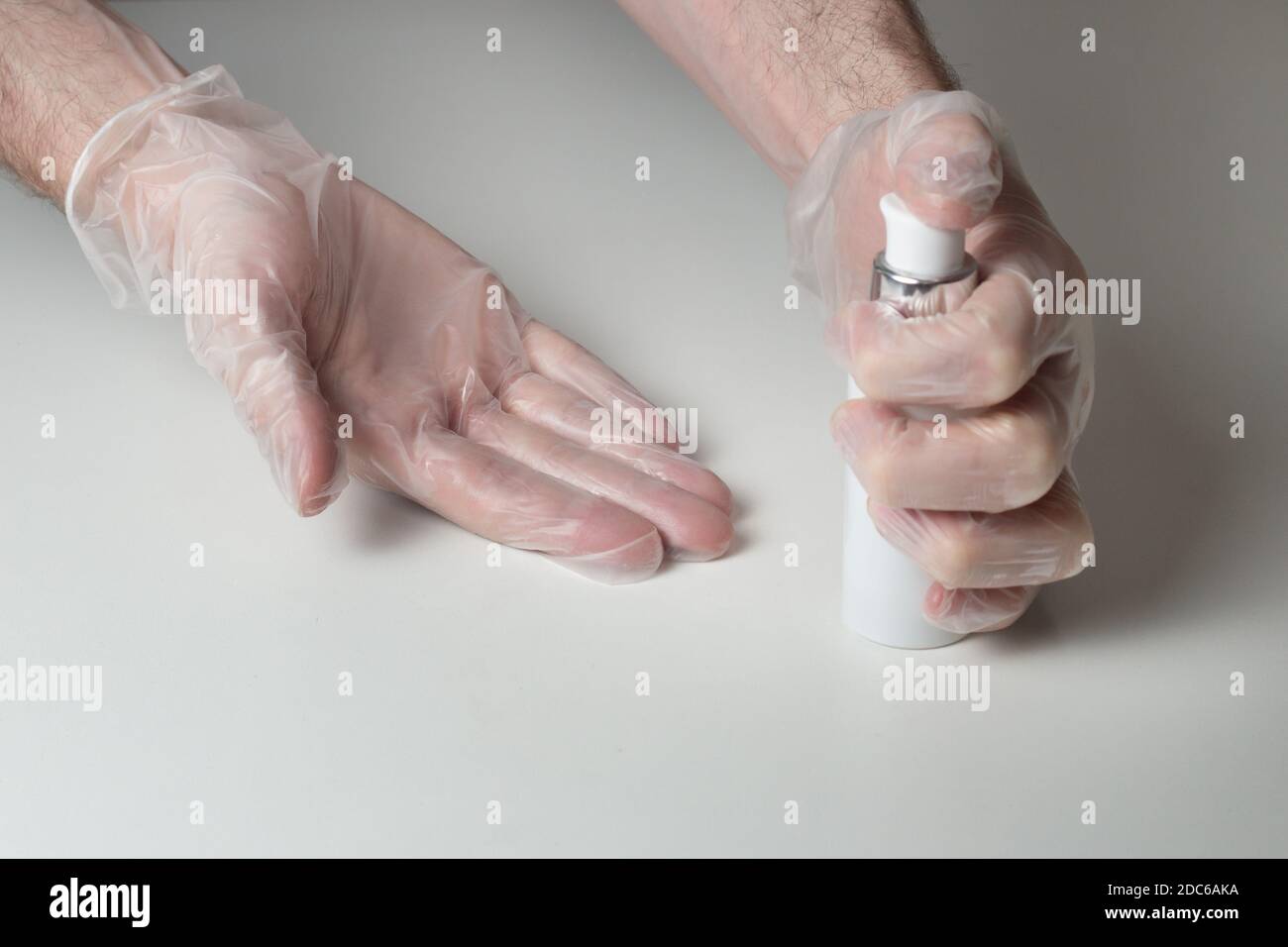 Eine Person, die kurz vor der Verwendung des Handdesinfektionsgels steht, um ihre Handschuhen zu reinigen. COVID-19. Schutzausrüstung auf einem weißen Tisch. Stockfoto