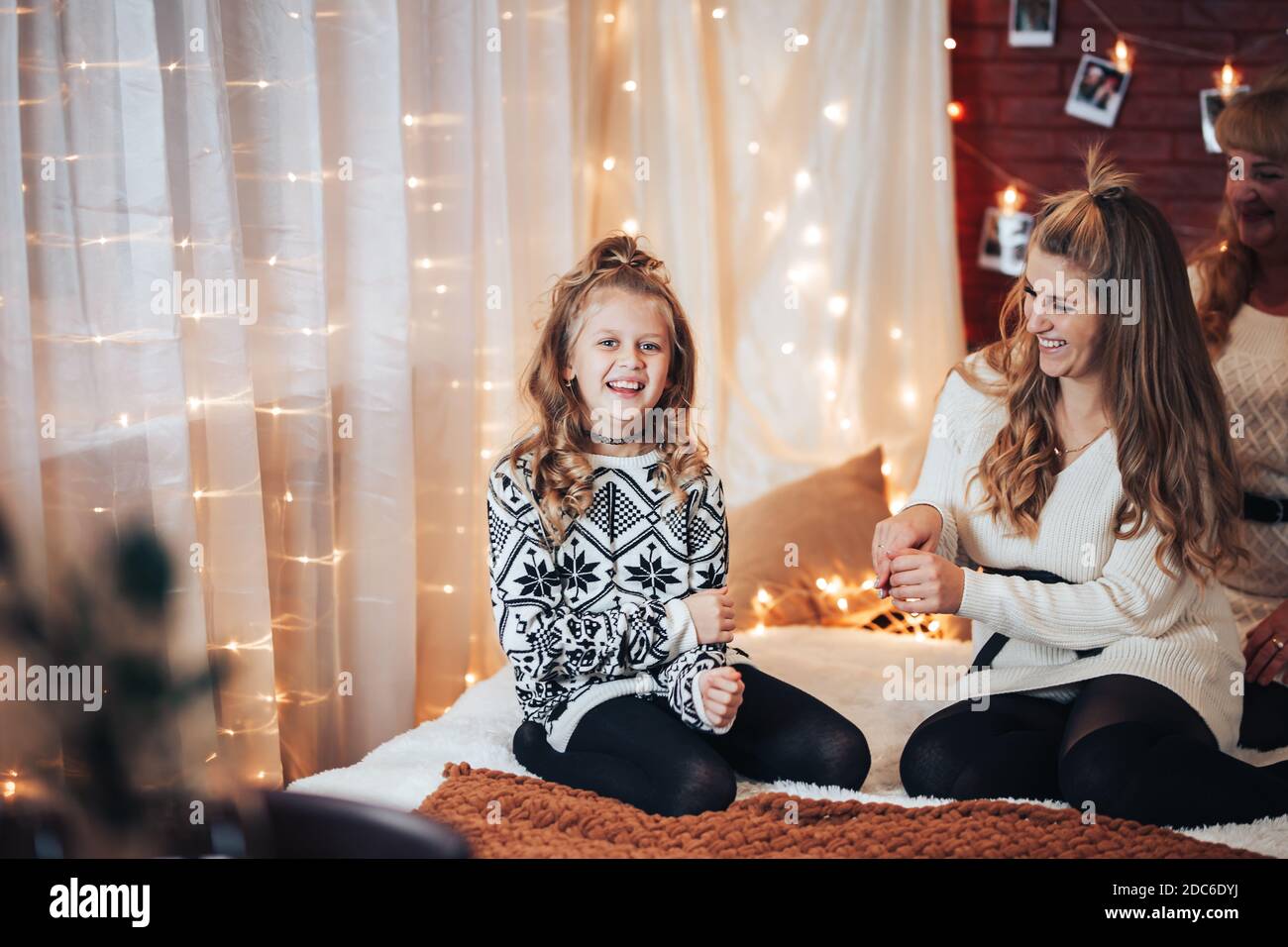 Mutter und Tochter sitzen auf dem großen Bett. Weihnachtsstimmung. Vor dem Hintergrund einer Backsteinmauer mit Girlanden. Stockfoto