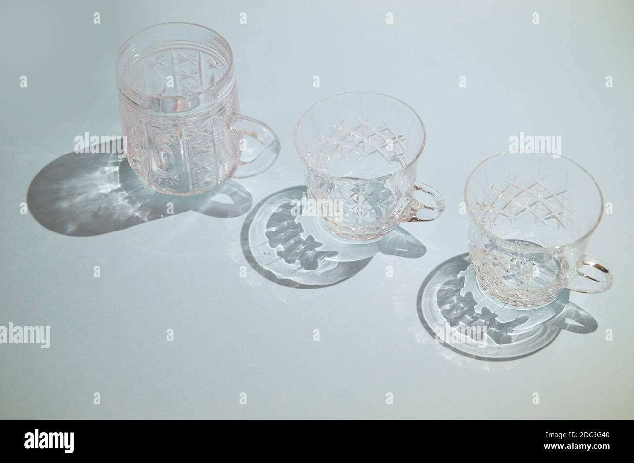 Drei kristallklare Tassen mit Griffen stehen in einer Reihe Auf blauem Hintergrund Stockfoto